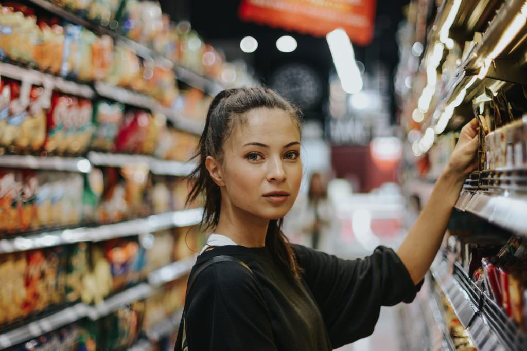 Dark haired woman reaching for a product on a shelf in a supermarket