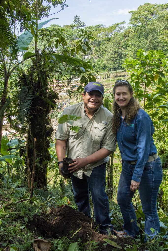 Two people smiling and holding a small sapling.