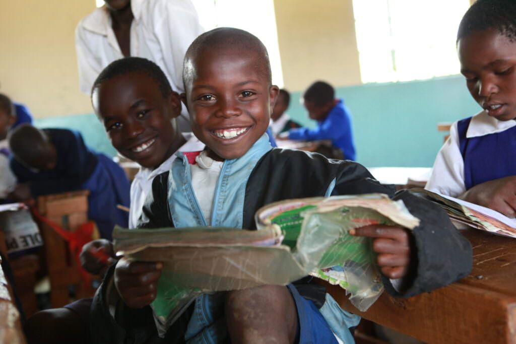 Student at Kericho HQ Primary School smiling while holding a book.