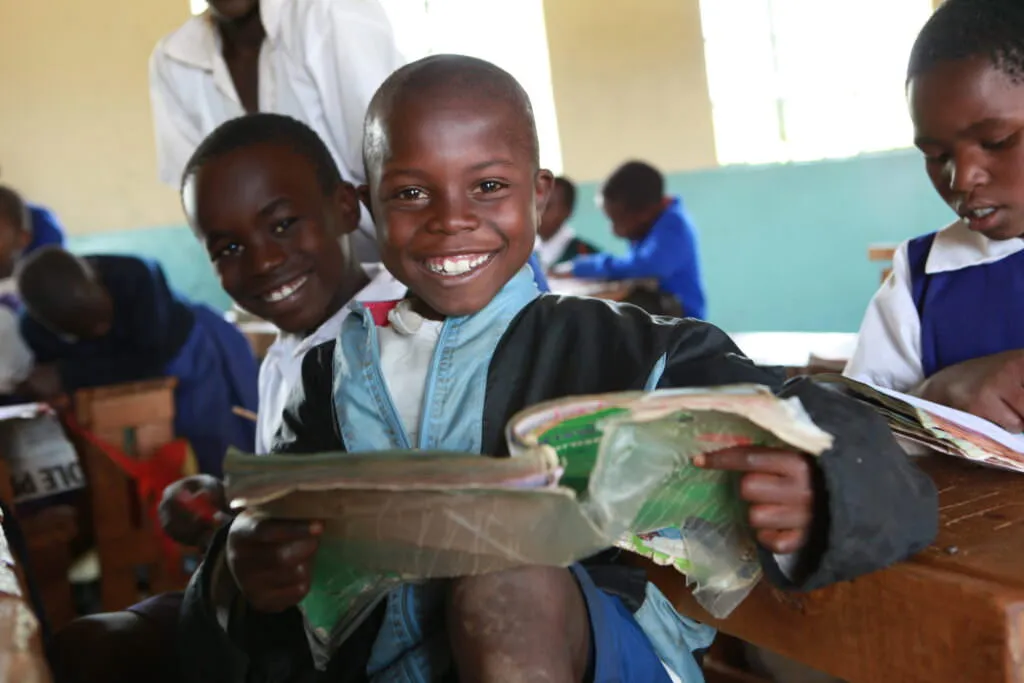 Student at Kericho HQ Primary School smiling while holding a book.