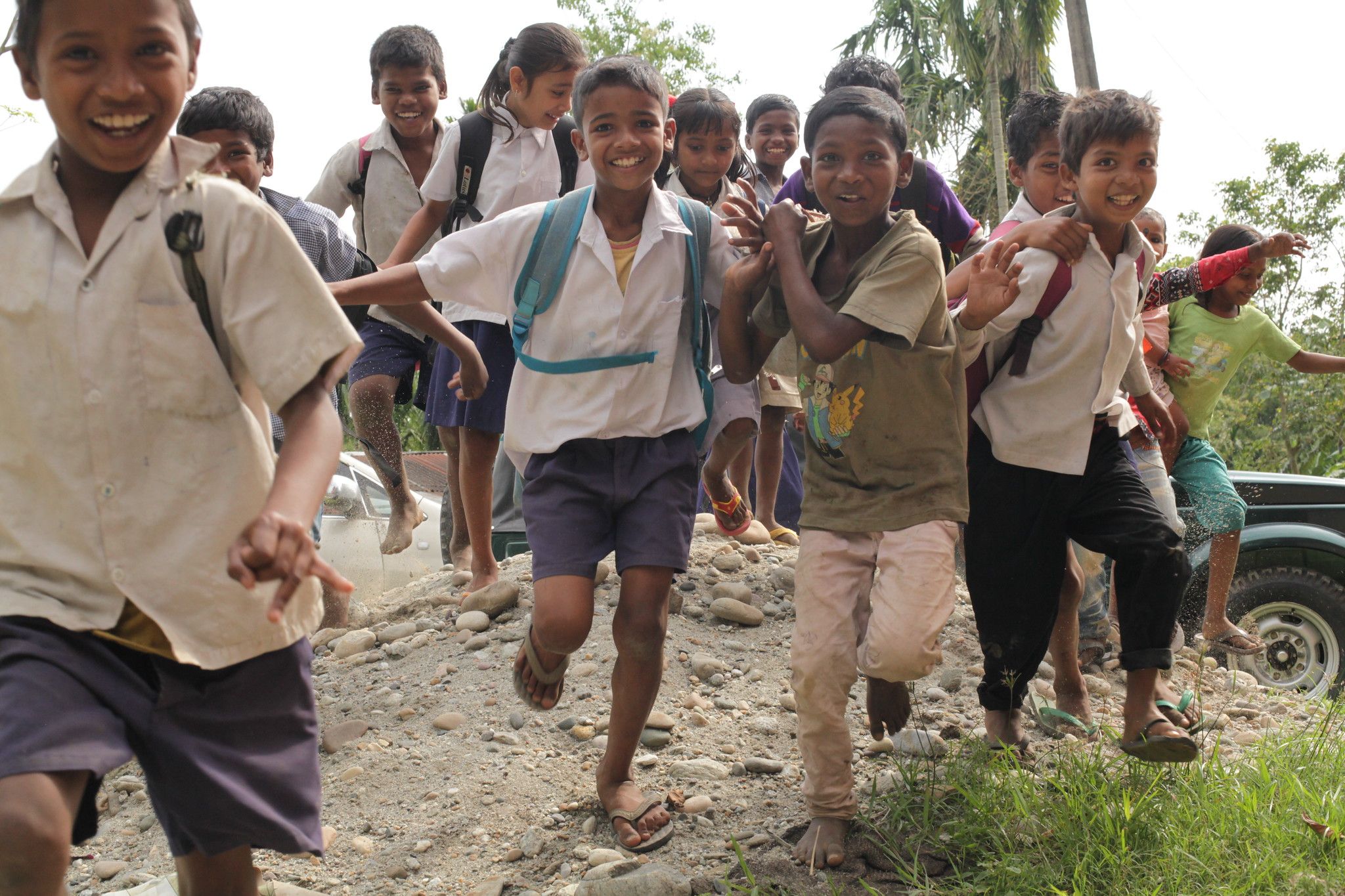 group of smiling schoolchildren run down a dirt road in Assam, India